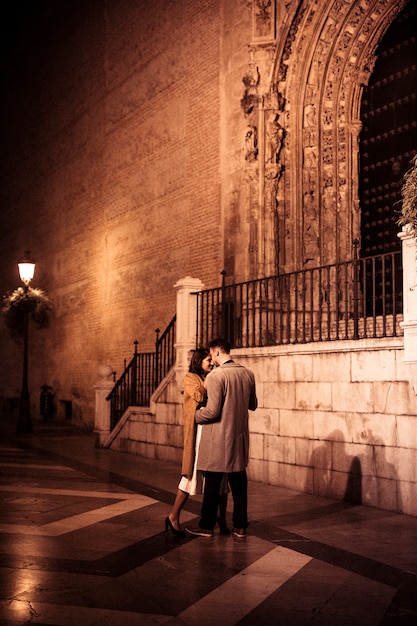 Señora elegante que abraza con el individuo joven en la calle por la tarde