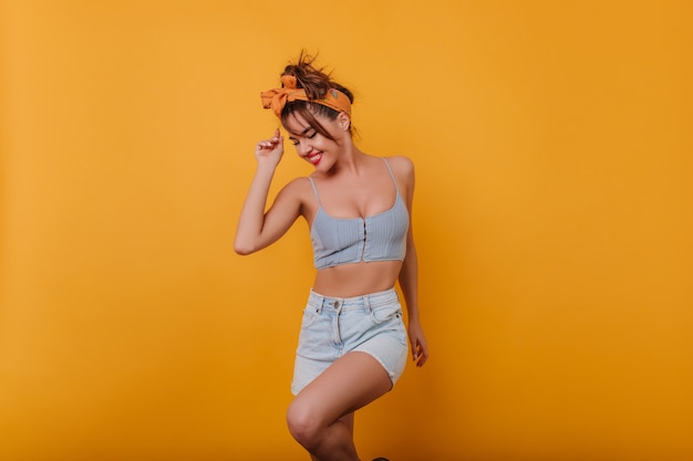 Señora encantadora con cinta naranja en cabello oscuro bailando con sonrisa