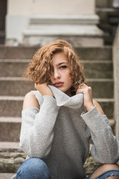 Foto gratuita señora encantadora con collar de suéter y sentado en pasos