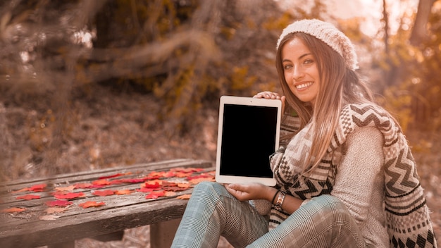 Foto gratuita señora encantadora que muestra la tableta junto a la mesa en el parque