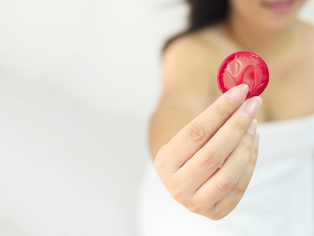 La señora está dando condón rojo, sexo seguro y concepto de anticoncepción.