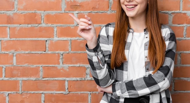 Señora feliz apuntando a la pared de ladrillo