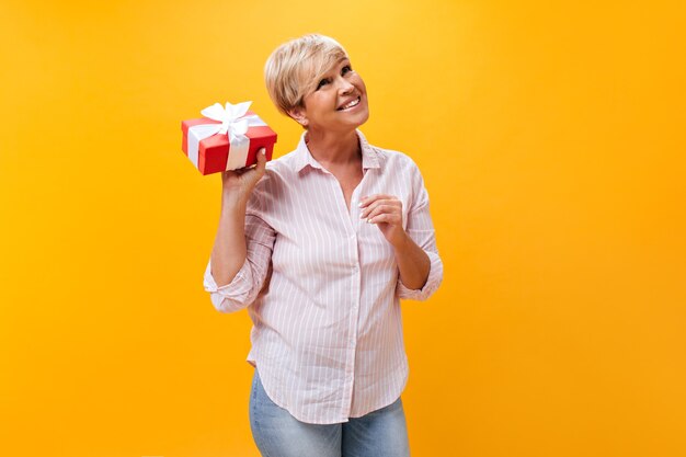 Señora feliz en camisa a rayas posando con caja de regalo