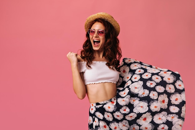 Señora feliz en falda elegante y navegante posando sobre fondo rosa mujer joven en falda colorida y sombrero grande es muy feliz en aislado