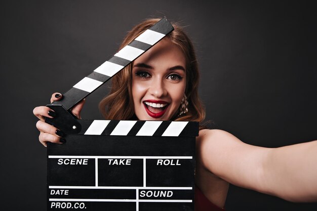 Señora feliz con hermoso maquillaje sosteniendo claqueta sobre fondo negro