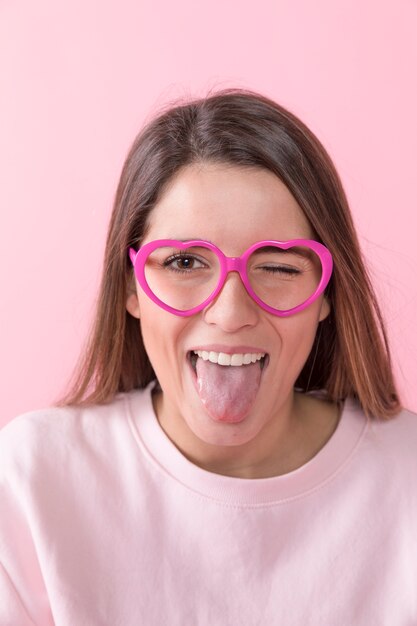 Señora feliz joven con las lentes que muestran la lengua