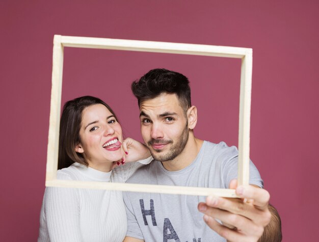 Señora feliz joven con la mano en el hombro del individuo positivo que lleva a cabo el marco de la foto