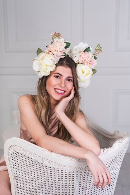 Señora feliz joven en vestido con las flores hermosas en la cabeza en el sofá