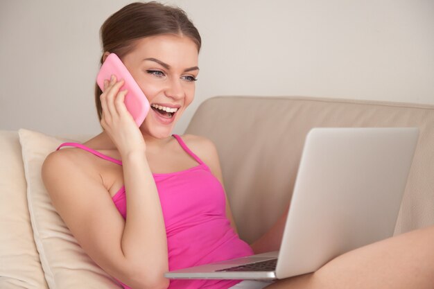 Señora feliz que habla en el teléfono celular mientras usa la computadora portátil
