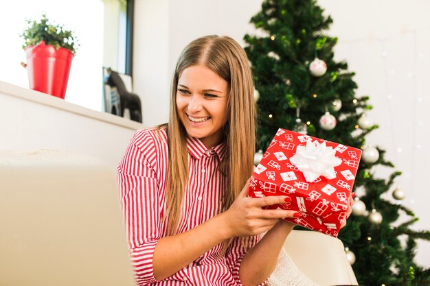 Señora feliz que sostiene la caja de regalo cerca del árbol de navidad