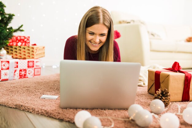 Señora feliz usando una laptop cerca de cajas de regalo y luces de colores