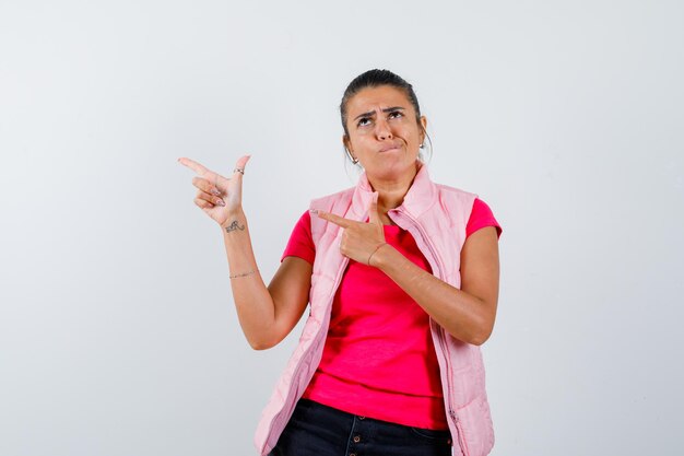 Señora haciendo signo de pistola de dedo en camiseta, chaleco y mirando vacilante