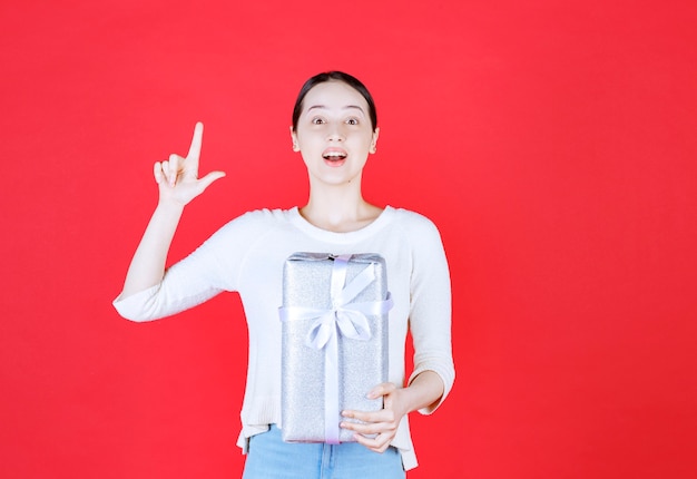 Señora hermosa joven que sostiene la caja de regalo en el dedo índice hacia arriba