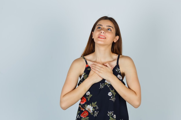 Señora joven en blusa cogidos de la mano en el pecho y mirando agradecido, vista frontal.