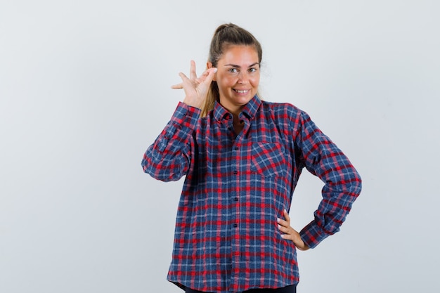 Señora joven en camisa a cuadros que muestra un gesto aceptable y que parece alegre, vista frontal.