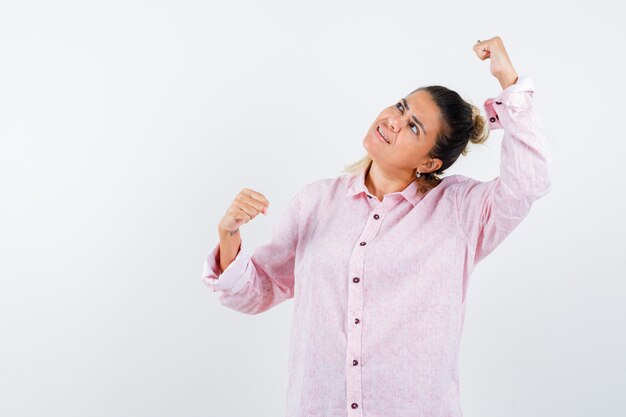 Señora joven en camisa rosa que muestra el gesto del ganador y parece feliz