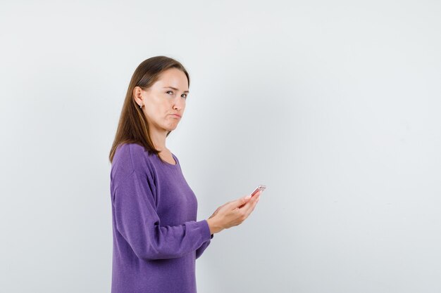 Señora joven en camisa violeta sosteniendo teléfono móvil y mirando pensativo.