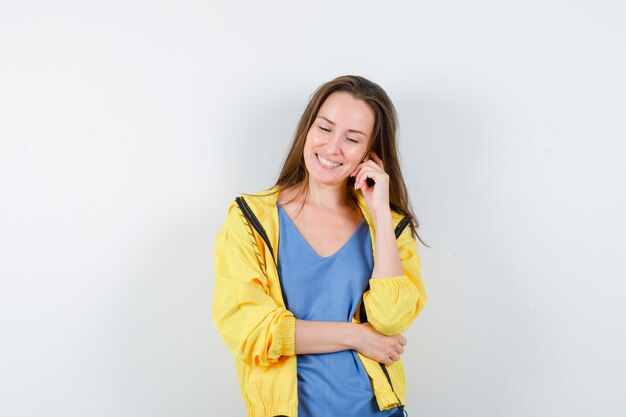 Señora joven en camiseta, chaqueta de pie en pose de pensamiento y mirando optimista, vista frontal.