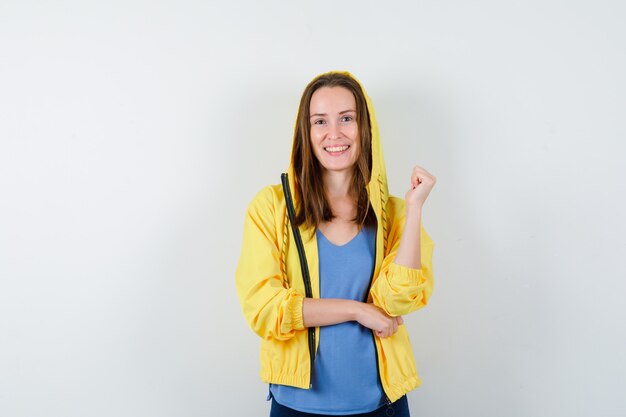 Señora joven en camiseta, chaqueta posando mientras está de pie y mirando alegre, vista frontal.