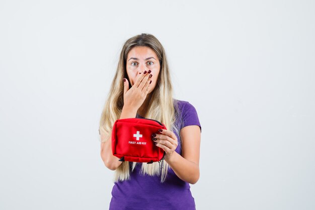 Señora joven en camiseta violeta con botiquín de primeros auxilios y mirando preocupado, vista frontal.