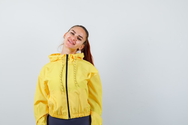 Foto gratuita señora joven en chaqueta amarilla posando mientras mira alegre, vista frontal.