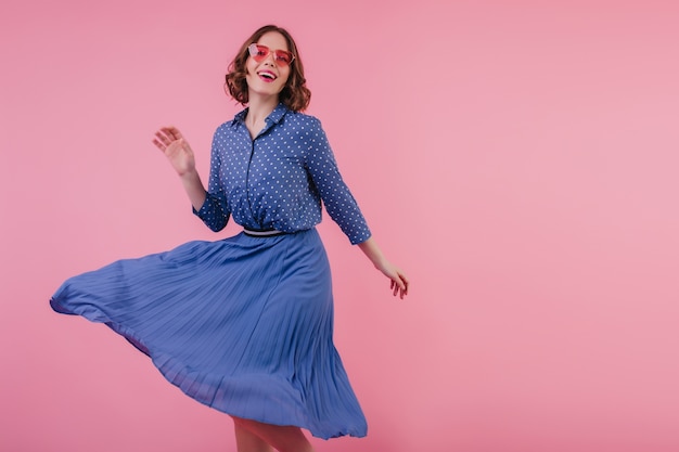 Foto gratuita señora joven complacida en blusa elegante bailando con bonita sonrisa. retrato de interior de niña rizada dichosa en falda midi relajante durante la sesión de fotos.