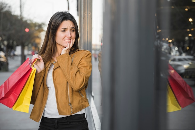 Señora joven confusa que sostiene bolsos de compras