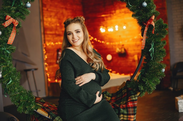 Señora joven elegante que se sienta cerca del árbol de navidad