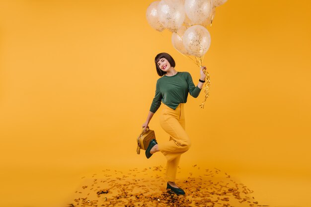 Señora joven extática relajante en cumpleaños y posando con placer. Retrato de atractiva chica caucásica divertida bailando con globos.