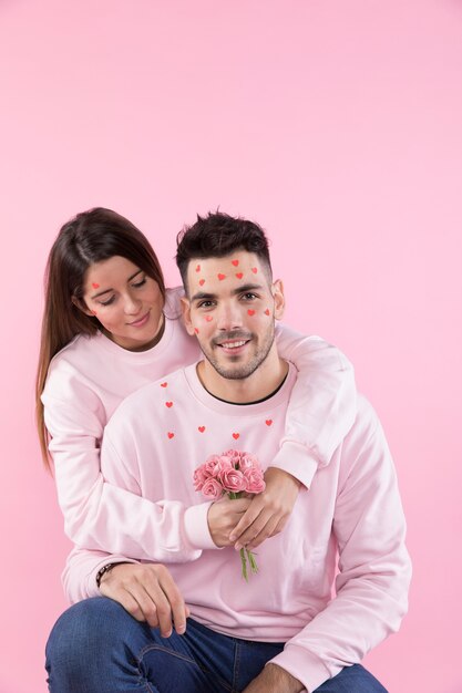 Señora joven con las flores que abrazan al individuo con los corazones de papel en cara