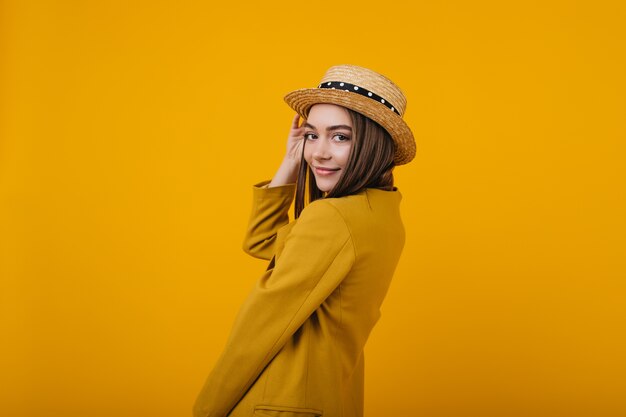 Señora joven linda en la chaqueta brillante de moda que presenta. Modelo femenino en sombrero de paja divirtiéndose