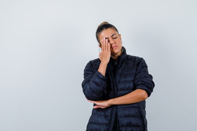 Señora joven con la mano en la cara en chaqueta acolchada y con aspecto cansado. vista frontal.