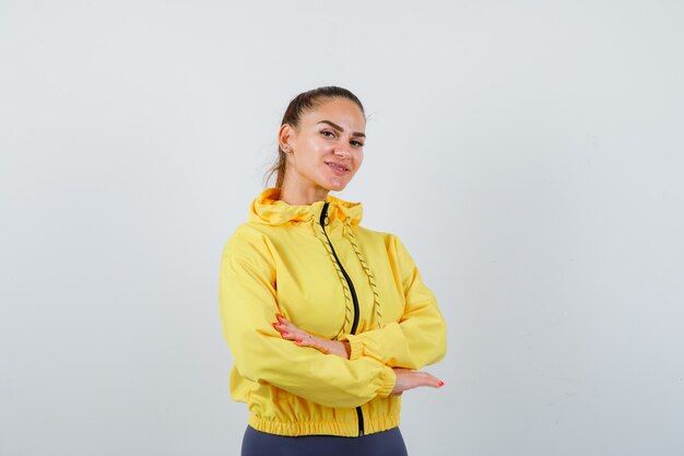 Señora joven con las manos cruzadas en chaqueta amarilla y mirando confiado. vista frontal.