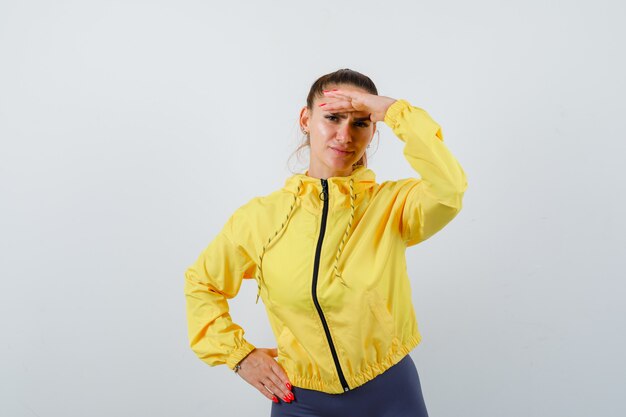 Señora joven con las manos sobre la cabeza en chaqueta amarilla y mirando pensativo. vista frontal.