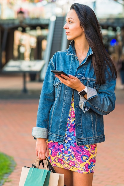 Foto gratuita señora joven con los paquetes de las compras que sostienen el teléfono móvil en centro comercial