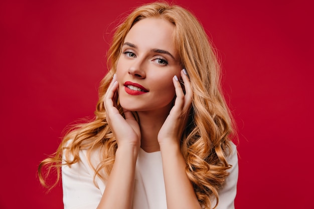 Señora joven positiva posando con sonrisa encantadora. alegre chica rubia aislada en la pared roja.