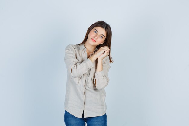 Señora joven que se inclina la cabeza en las manos entrelazadas en casual, jeans y parece confiada. vista frontal.