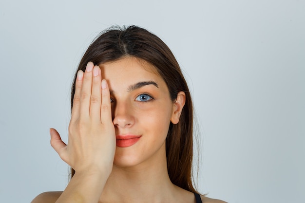 Señora joven que lleva a cabo la mano en el ojo y que parece alegre. vista frontal.