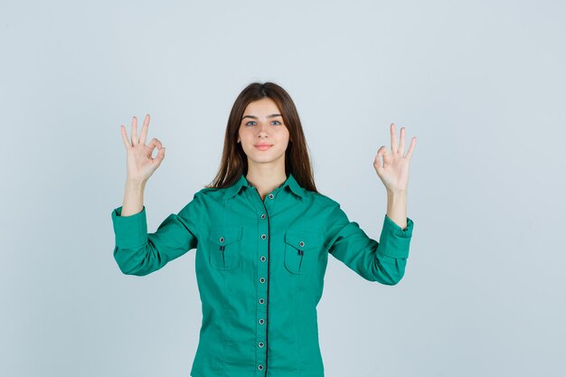 Señora joven que muestra un gesto aceptable en camisa verde y que mira confiada, vista frontal