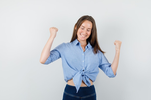 Señora joven que muestra el gesto del ganador en camisa azul, pantalones y que parece feliz.