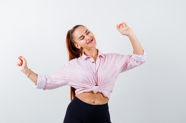 Señora joven que muestra el gesto del ganador en camisa, pantalones y que parece feliz. vista frontal.