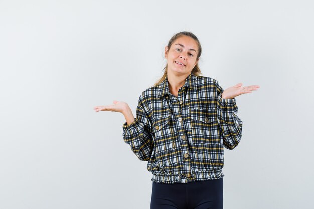 Señora joven que muestra un gesto de impotencia en camisa, pantalones cortos y que parece confundido. vista frontal.