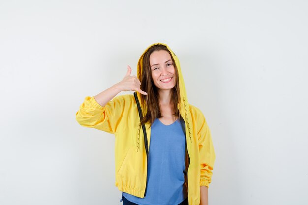 Señora joven que muestra el gesto del teléfono en camiseta, chaqueta y que parece seguro. vista frontal.