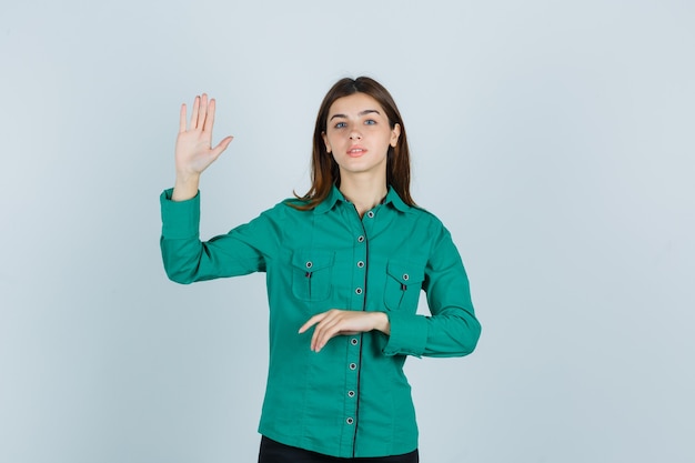 Señora joven que muestra la palma en camisa verde y que mira confiada, vista frontal.