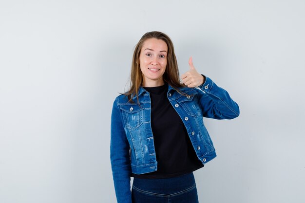 Señora joven que muestra el pulgar hacia arriba en camisa, chaqueta y parece confiada. vista frontal.