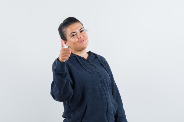 Señora joven que muestra el pulgar hacia arriba en la chaqueta y parece optimista. vista frontal.