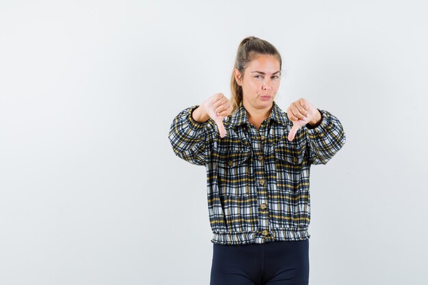 Señora joven que muestra el pulgar doble hacia abajo en camisa, pantalones cortos y mirando confiado, vista frontal