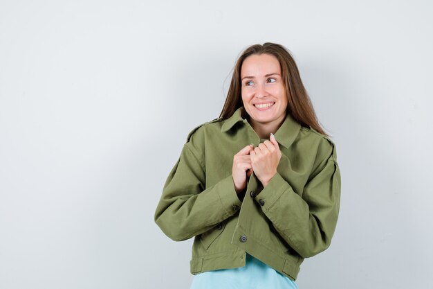Señora joven que sostiene la chaqueta mientras mira a otro lado en camiseta, chaqueta y se ve alegre. vista frontal.