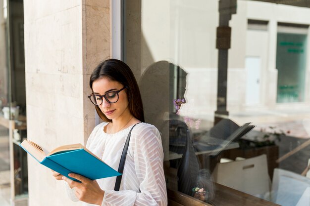 Señora joven que sostiene el libro cerca de ventana