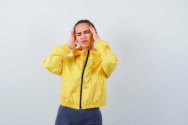 Señora joven que sufre de dolor de cabeza en chaqueta amarilla y parece doloroso. vista frontal.